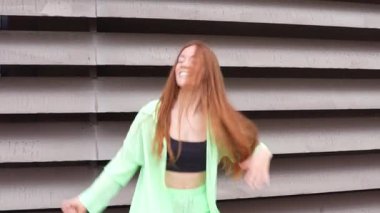 Hareketli şehirde, neşeli kızıl saçlı bir kadın neşeli bir şekilde çağdaş bir binanın yanında dans ediyor, özgürlük ve mutluluğu canlandırıyor, hayat dolu kişiliğini yansıtan hareketli bir ortam yaratıyor.