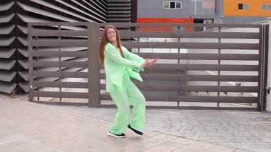 Kaygısız genç bir kadın, neon yeşili giyinmiş, enerjik bir şekilde şehirde dans ediyor, neşeli ifadesi ve hareketleriyle son moda bir şehir tarzı sergiliyor, özgürlük ve enerji saçıyor.