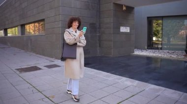 Şık bir kadın, akıllı telefonuna dalmış, çağdaş hayatı somutlaştıran yoğun bir kaldırımda güven içinde yürür. Bu sahne modern zarafetle yaşam tarzını ve moda temalarını mükemmel bir şekilde gözler önüne seriyor.