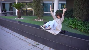 Rahat bir birey açık havada güneşli ve parlak bir günün tadını çıkarıyor. Çevrelerindeki yemyeşil yemyeşil yemliklerle çevrili canlı bir kentsel çevredeki modern taş bir bankta rahatça oturuyor.