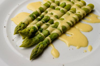 Beyaz tabakta servis edilen soslu yeşil kuşkonmaz.