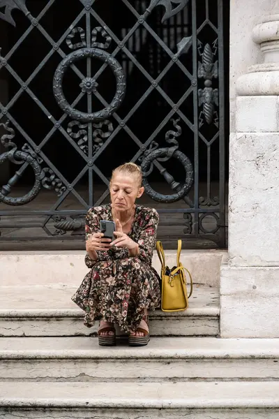 Vicenza, İtalya - 12 Ağustos 2024: Loggia del Capitaniato Merdivenlerinde Oturan ve Akıllı Telefonunda okuyan İtalyan Kadın.