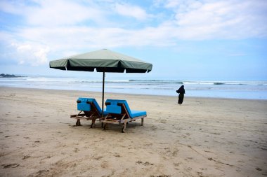 Bali 'deki Kuta Plajı' nda Şemsiye Şemsiyesi, Plaj Salonu ve tesettürlü Koşan Müslüman Kadın