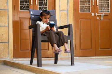 Jaisalmer, Rajasthan, Hindistan - 12 Şubat 2025: Cep Telefonu Üzerinde Oynayan Hintli Kız, Sandalyede Oturan