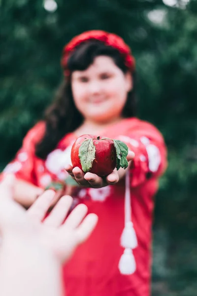 A girl in red gives a red apple to another girl. Presented apple.