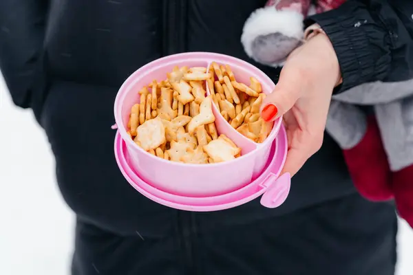 Bir kadının eli pembe bir kutu kraker tutar. Atıştırmalık temiz hava. 