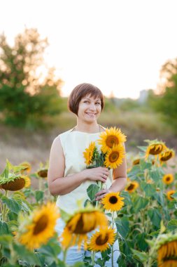 Doğanın tadını çıkaran güzel, genç bir esmer. Ayçiçeği tarlasında elinde buketle mutlu bir esmer.. 