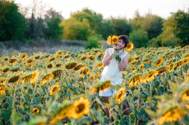 Doğanın tadını çıkaran güzel, genç bir esmer. Ayçiçeği tarlasında elinde buketle mutlu bir esmer.. 
