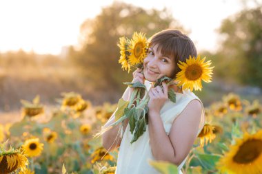 Doğanın tadını çıkaran güzel, genç bir esmer. Ayçiçeği tarlasında elinde buketle mutlu bir esmer.. 