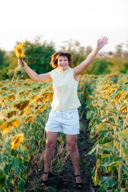 Doğanın tadını çıkaran güzel, genç bir esmer. Ayçiçeği tarlasında elinde buketle mutlu bir esmer.. 