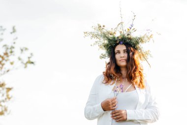Beyaz çiçekli bir çelenk içinde esmer. Makyajsız bir kadın hayattan zevk alır. Doğada meditasyon. Kadın ve doğa. 