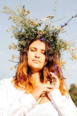 Beyaz çiçekli bir çelenk içinde esmer. Makyajsız bir kadın hayattan zevk alır. Doğada meditasyon. Kadın ve doğa. 