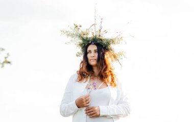 Beyaz çiçekli bir çelenk içinde esmer. Makyajsız bir kadın hayattan zevk alır. Doğada meditasyon. Kadın ve doğa. 