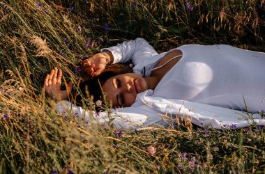 Esmer kadın çimlerin üzerinde dinleniyor. Doğada meditasyon. Doğayla etkileşim. Vahşi çiçeklerin arasındaki kadın. 