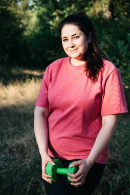 A plus-size woman doing dumbbell exercises outdoors. Outdoor sports. Green dumbbells in the athletes hands. High quality photo