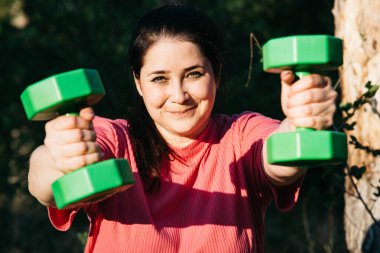 A plus-size woman doing dumbbell exercises outdoors. Outdoor sports. Green dumbbells in the athletes hands. High quality photo
