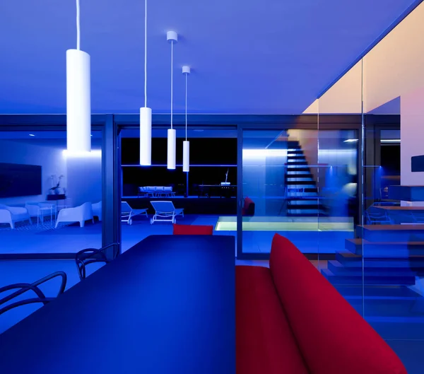 テーブル付きのフロントビューリビングルームと天井に取り付けられた青いLedとランプによって照らされた赤いソファ プールと庭を見下ろす大きな窓 誰も中に — ストック写真