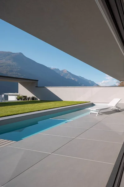 Garden of modern villa with swimming pool and a deck chair for relaxing. Sunny day in the Alps of Switzerland. Nobody inside