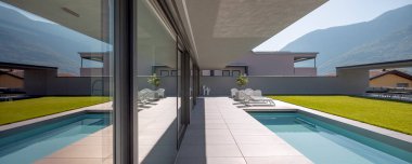 Manikürlü yeşil bahçesi olan modern bir ev, gölgeli bir avlu. İki güverte sandalyeli havuz ve beyaz koltuklu küçük bir salon. İsviçre Alpleri 'nin manzarası. İçeride kimse yok.
