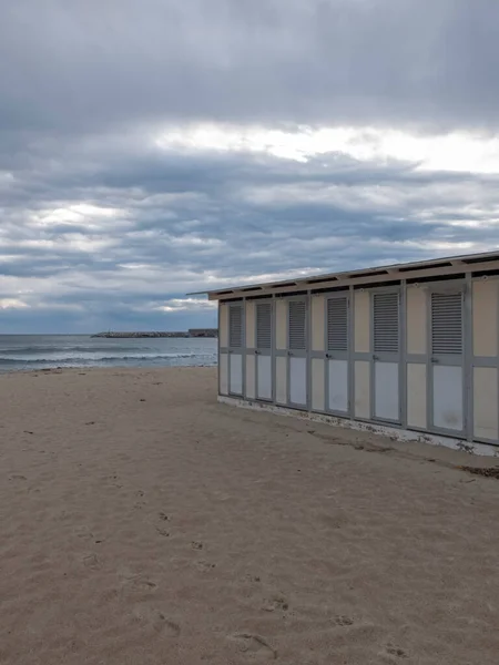 Deserted Italian beach, no one around, we are towards evening with a cloudy sky. On the right you can see the closed cabins.