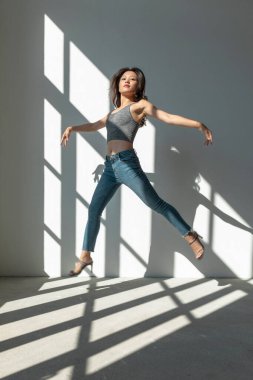 Asyalı dansçı kız, boş bir binanın camından içeri giren güneşin aydınlattığı akrobatik bir atlayış yapıyor. izole