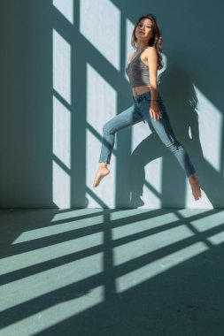 Asyalı dansçı kız, boş bir binanın camından içeri giren güneşin aydınlattığı akrobatik bir atlayış yapıyor. izole