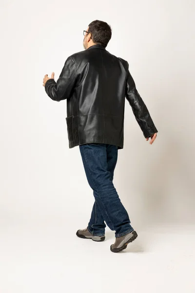 Isolated man on white background is standing and walking to the back. He is wearing a leather jacket and blue jeans. Copy space