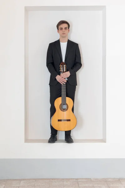 エレガントなスーツの少年が壁のニッチに立っている 両手でギターを持っている 白地に隔離された — ストック写真