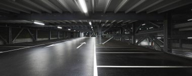 Sahneyi aydınlatan lambaları olan modern yeraltı garajı. Otopark çizgileri yere çizilmiş. İçeride kimse yok.