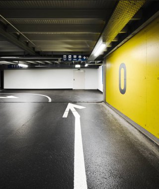 Zeminde ok olan modern yeraltı otoparkı. Yön ve zemin numarası yazılı sarı bir duvar. İçeride kimse yok.