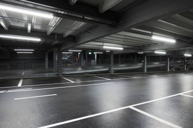 Sahneyi aydınlatan lambaları olan modern yeraltı garajı. Otopark çizgileri yere çizilmiş. İçeride kimse yok.