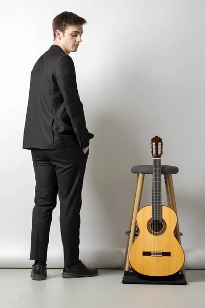 Jeune Garçon Costume Noir Regarde Guitare Appuyée Sur Tabouret Côté — Photo