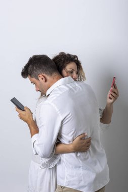 Bir kadın ve bir erkek akıllı telefonlarına bakarken birbirlerine sarılırlar. Bu çiftler arasında sosyal bir sorundur. Beyaz arkaplan, stüdyo çekimi