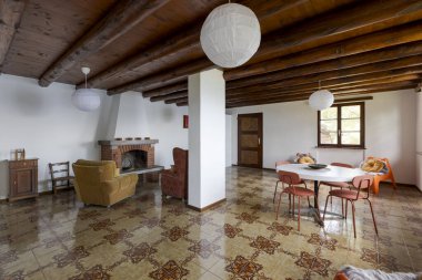 Şöminesi olan büyük bir oturma ve yemek odası. Eski ve modası geçmiş mobilyalar var. Dağlarda bir tatil evi