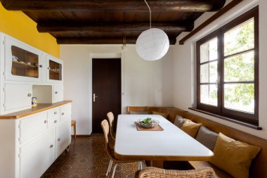 Boş yemek odası, sadece bir masa, sandalyeler ve bir bank. Solda tabak ve bardaklar için bir dolap..