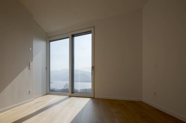 Ahşap zemini olan modern bir apartmanın içinde. Pencereden akan güneş ışığı İsviçre 'nin dağları ve gölünün resimli bir manzarasını sağlıyor. Kimse yok..