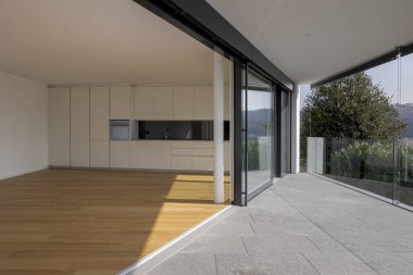 Duvarına mutfak ve ahşap zemin bağlı büyük boş yemek odası. Yer boş ve bitişik teras üçgen. Bu modern bir mimari ve pencere açık..