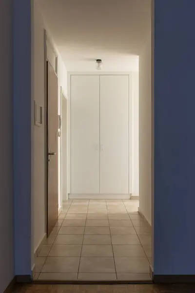 Hallway with white walls and tiles. At the end there is a closed wardrobe. Nobody inside