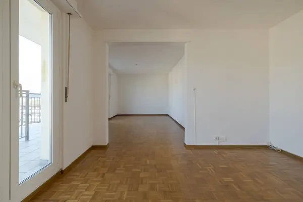 Front view of an empty room with windows for natural light. Parquet floor. No one inside
