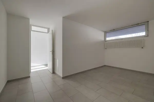 Room with white walls and a small window and an open door leading to the corridor. Nobody inside