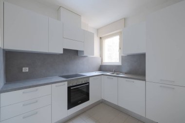 Beyaz kapıları ve gri kapağı olan yeni yenilenmiş bir mutfak. Çok parlak bir pencere var. İçeride kimse yok.