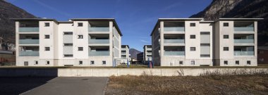 Bahçesi ve çocuklar için oyunları olan bir konut kompleksinin önü. Mavi gökyüzü var, içinde kimse yok.