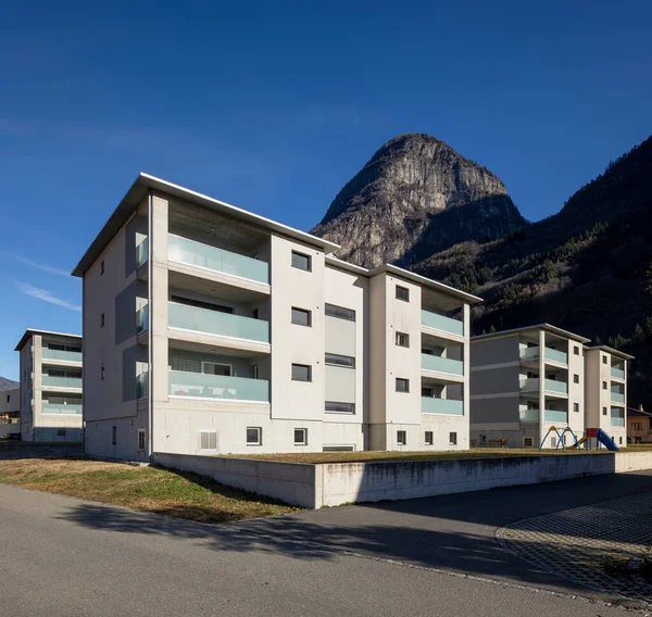 Bahçeli, çocuklar için oyunlar ve arabalar için park yeri olan bir site. Mavi gökyüzü ve dağlar var, içeride kimse yok.