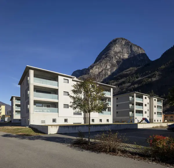 Bahçeli, çocuklar için oyunlar ve arabalar için park yeri olan bir site. Mavi gökyüzü ve dağlar var, içeride kimse yok.