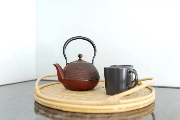 在明亮的厨房里 一只红色的中国茶壶和两只黑色杯子的细部放在柳条盘上 里面没有人 图库图片