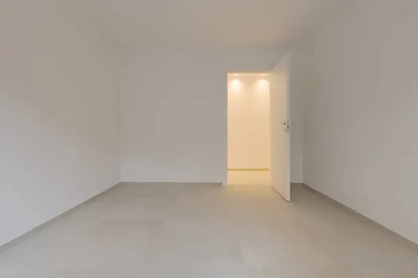空っぽの部屋と右側のドアの内側には 光が点灯して廊下につながっています すべての壁と天井は白い ストック写真