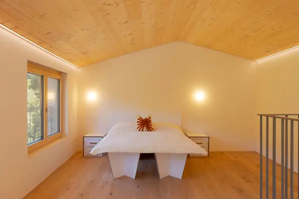 stock image Home staging bedroom with cardboard furniture, bed and two bedside tables. Above the bed is a pillow. There is a window with a view of nature and LED strips on the ceiling. Nobody inside