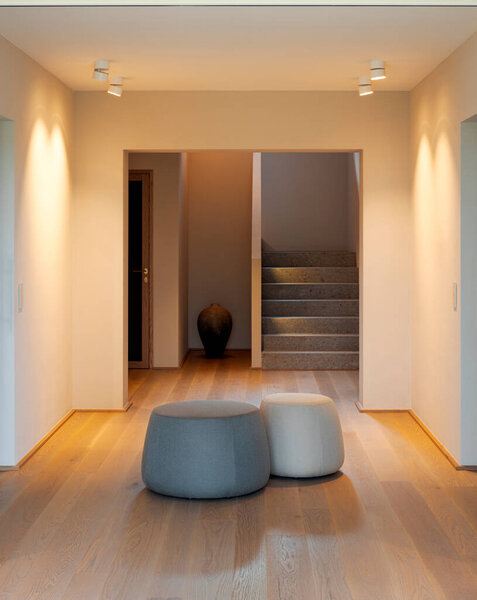 Интерьер очень похожего на озеро коридора с лестницей на заднем плане. Пол паркет, а в середине два оттомана для сидения.