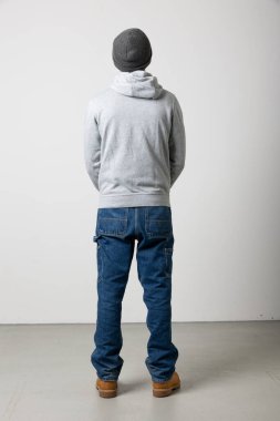 Gri kazaklı ve kotlu sıska bir çocuk. Arkadan görülmüş. Tüm vücudu beyaz arka planda izole edilmiş. Orada dikiliyor ve önüne bakıyor. Yüzünü göremezsin.