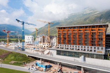 Mavi bulutlu bir yaz gününde Andermatt, Canton Uri 'deki dağ köyünde şantiyesi olan bir turizm merkezi. Fotoğraf 21.08.2024 Andermatt, İsviçre. Arka planda birçok vinç; şimdilik, büyük bir inşaat alanı, ama gelecekte, 